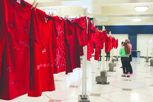 Students walk amongst the rows of t-shirts chronicling domestic and sexual assault at the Clothesline Project.
