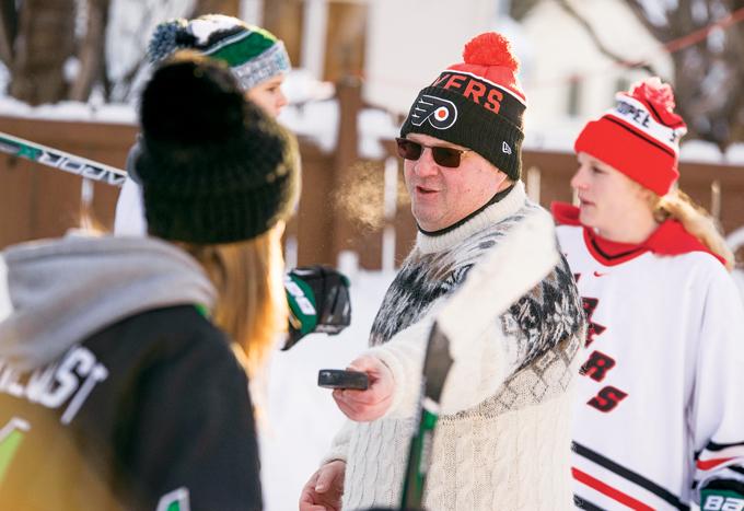 Peter Elander (center), associate head coach of the UND women's hockey team and host of the Winter Classic, hands a puck to forward Charly Dahlquist Monday afternoon at his backyard ice rink called 'Peter's Ice Palace.'