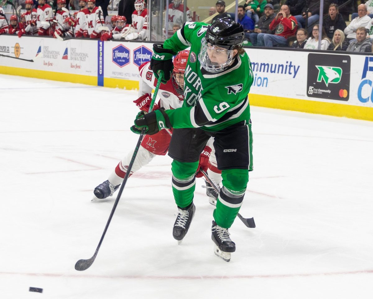 UND's Will Zellers sends a puck toward Matteo Drobac during a game.